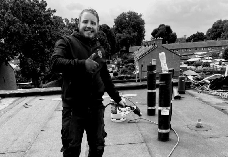Leonard Jansen aan het werk op een plat dak, met brander en rollen dakbedekking